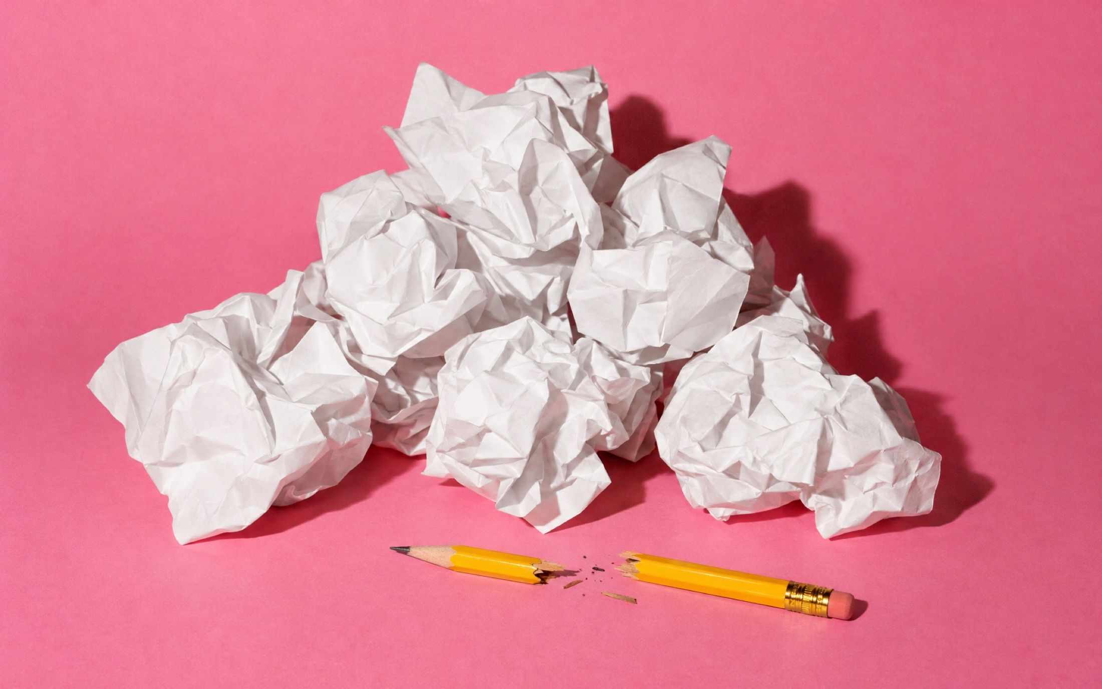 A heap of crumpled paper and a broken pencil on a pink backdrop