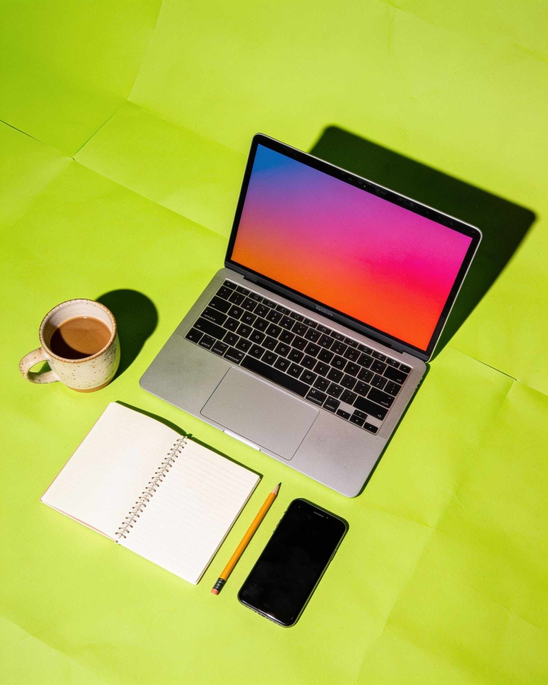 A laptop, notebook, coffee cup and phone from above on lime paper