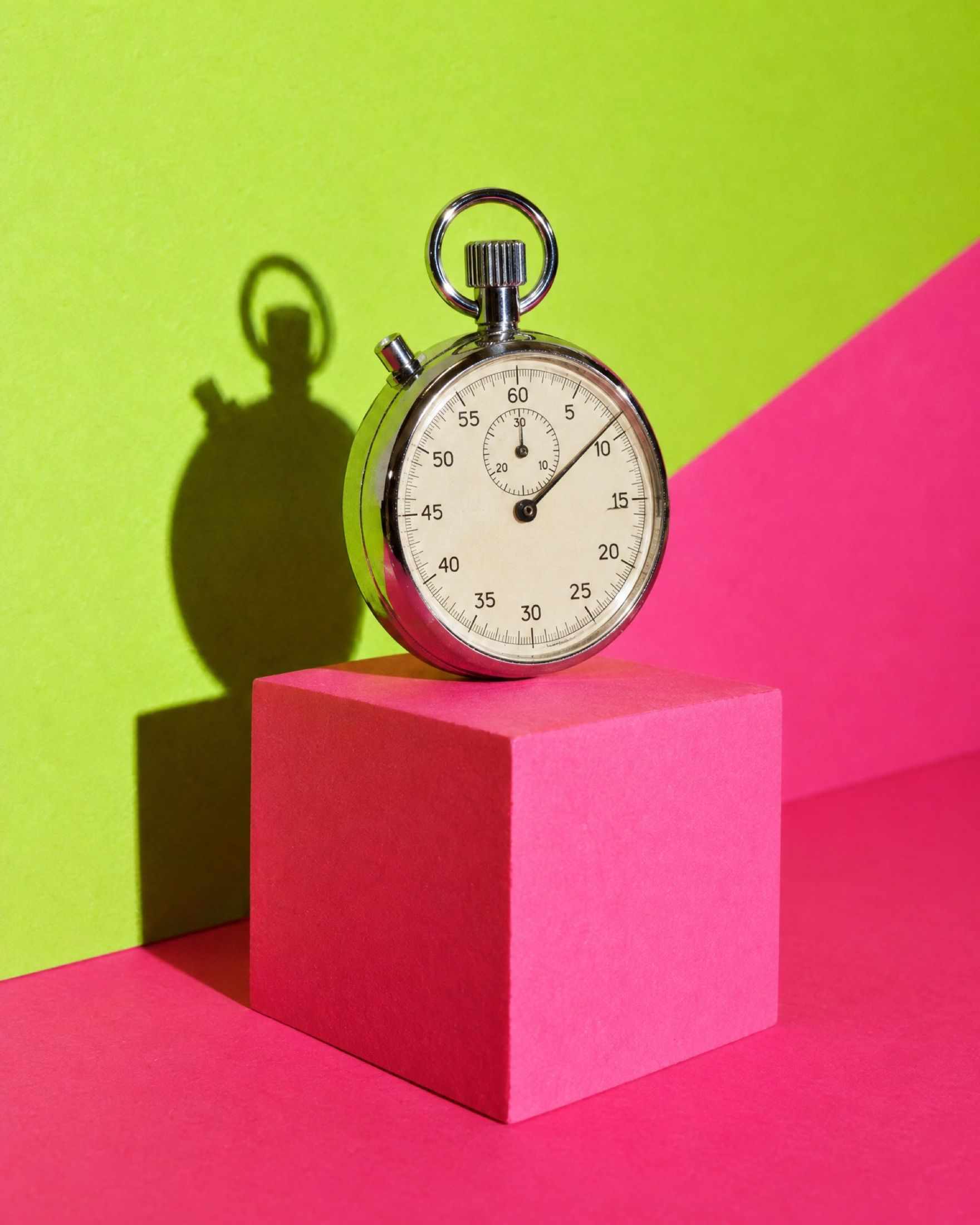 A vintage stopwatch standing on a block against lime and pink paper