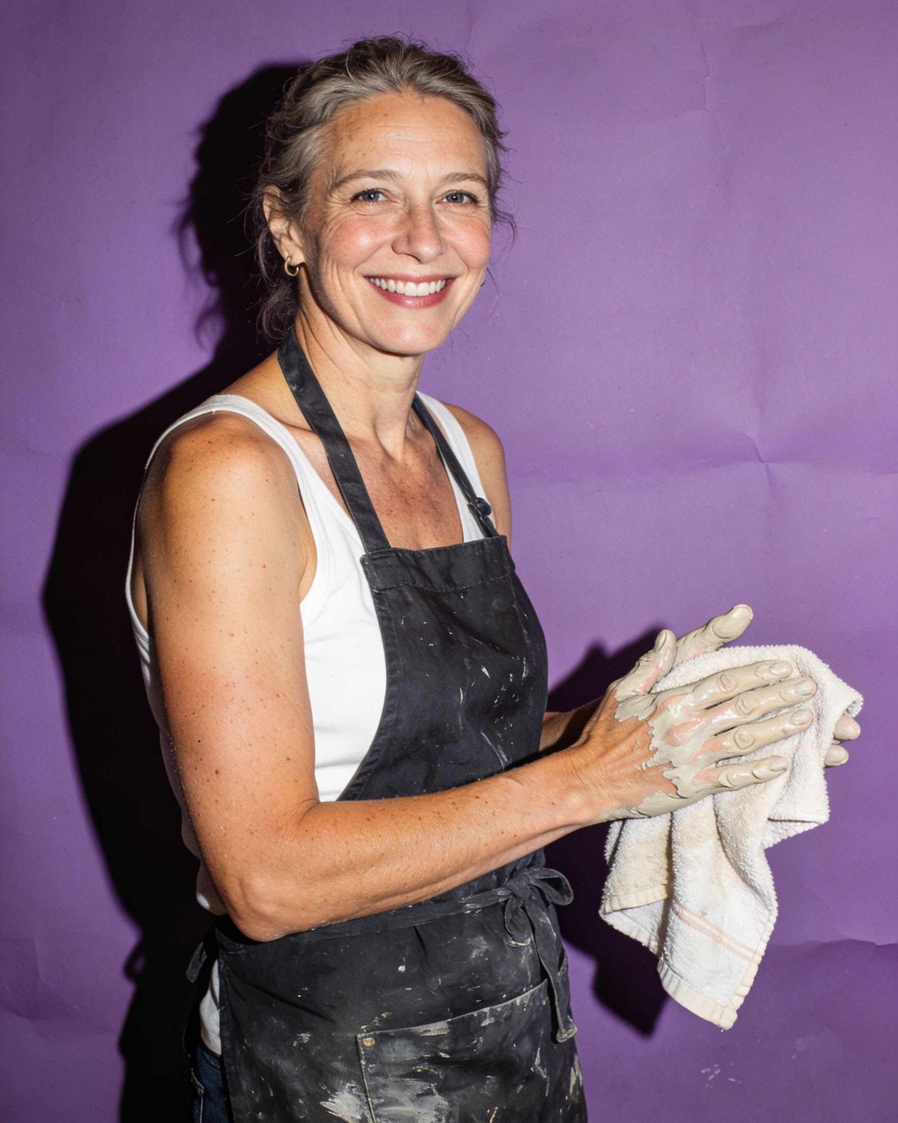 A smiling ceramicist wiping clay off her hands on a lilac backdrop