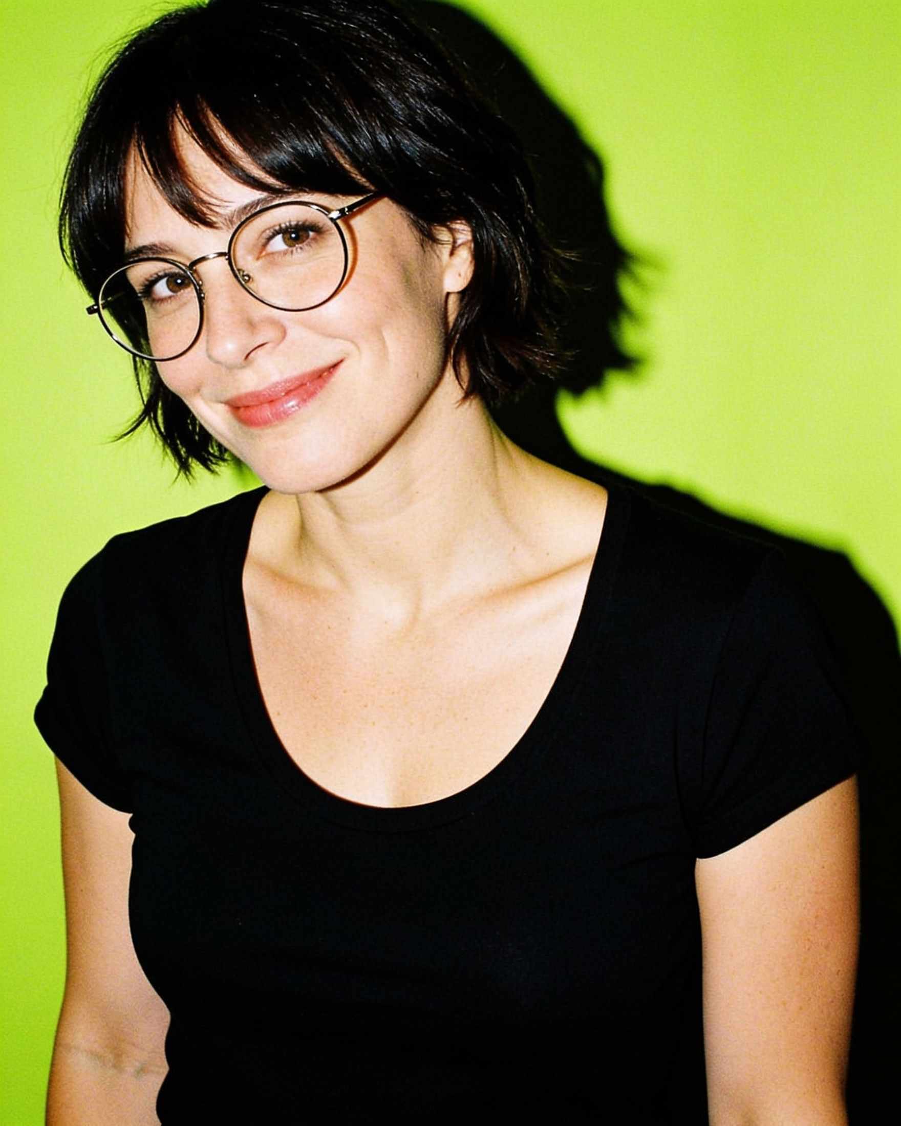 Nora, a woman with short dark hair and round glasses, on a lime backdrop